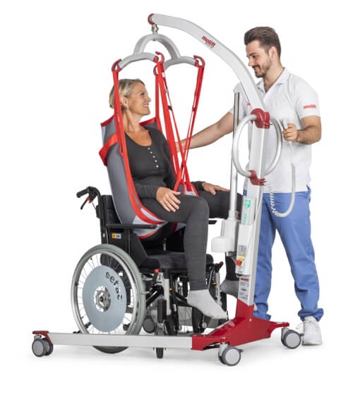 Molift Mover 180 hasta taşıma lifti. tekerlekli sandalye kullanıcısı bir kadını bir hasta bakıcı adam liftle sandalyesinden kaldırmış. 