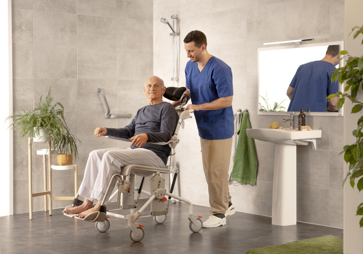 Swift mobile tilt banyo tuvalet sandalyesi . Yaşlı bir adam sandalyeye oturmuş,, erkek bir hasta bakıcı arkasında onu. itiyor. Banyodalar.